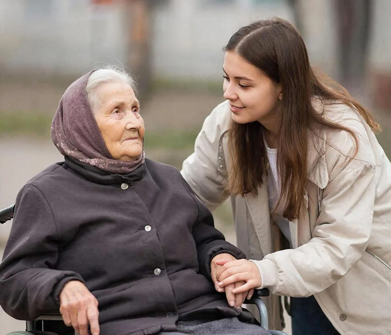 на фото пожилая женщина на коляске и рядом девушка.